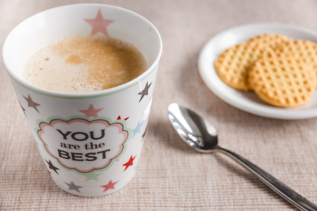 A coffee mug that says "You are the best" next to a spoon and a plate of cookies