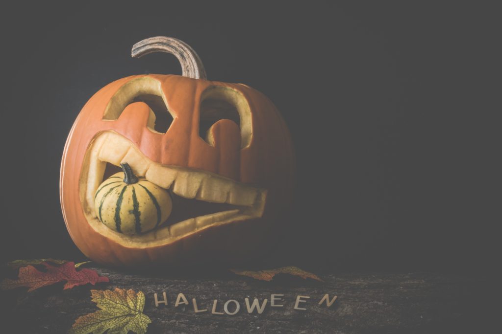 jack o' lantern with a smaller pumpkin in its mouth on a wooden surface with the word Halloween in capital letters on the wood