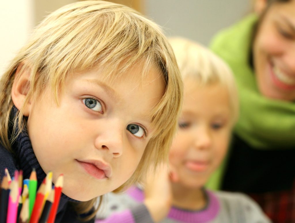 a young blonde girl sitting next to another girl and near some colored pencils