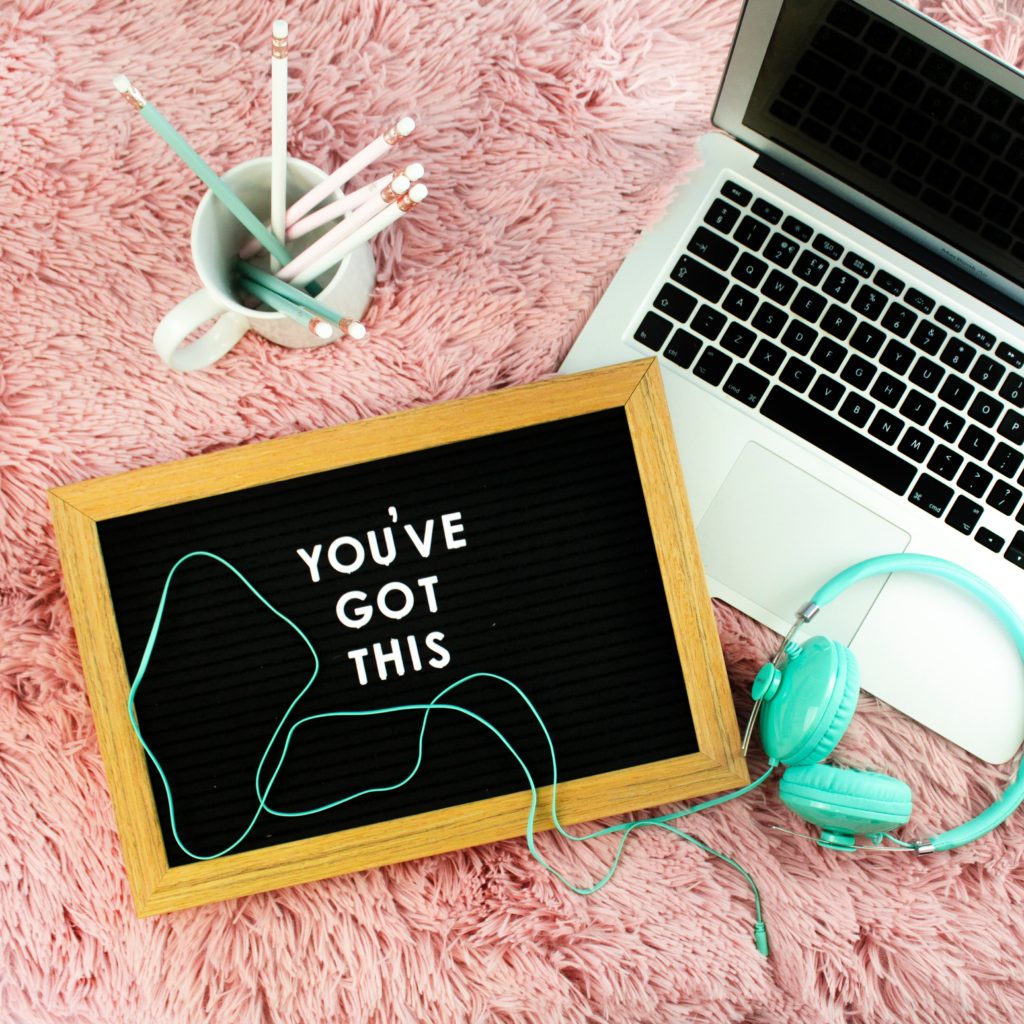 A board that reads "YOU'VE GOT THIS" next to a laptop, pencil cup, and headphones