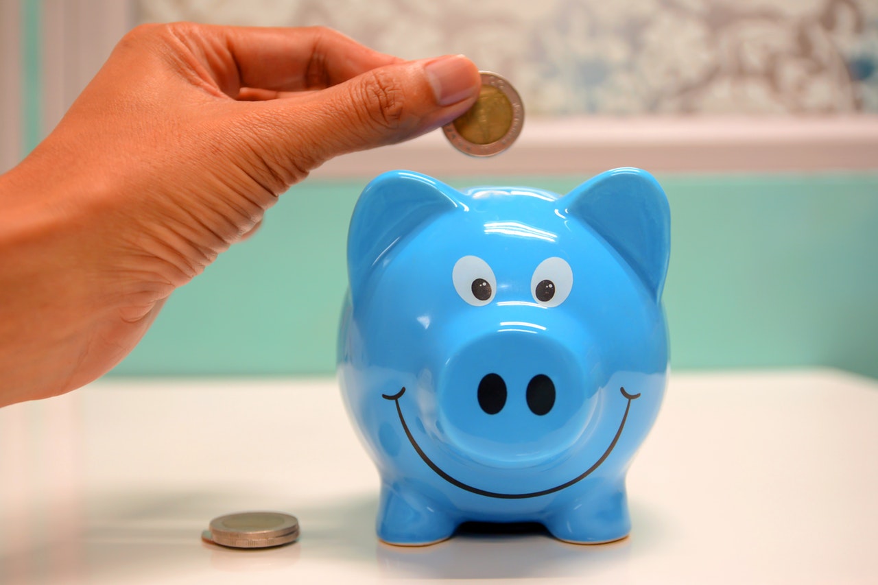 Person placing a coin into a blue piggy bank