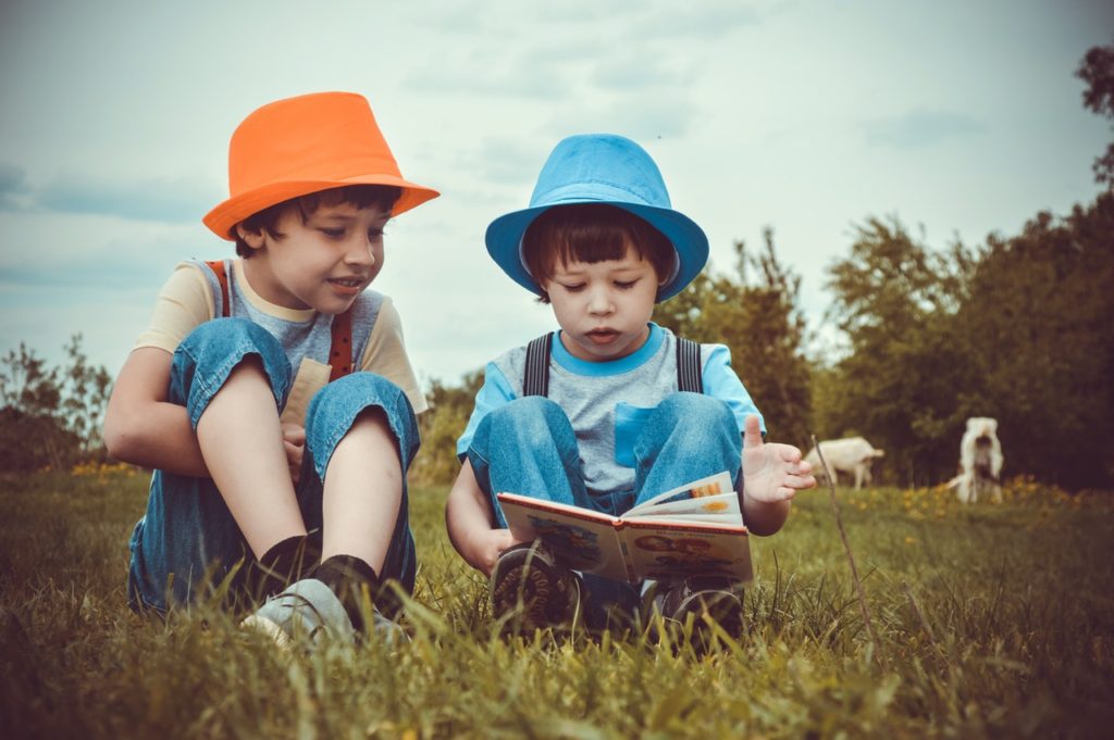 Two children sitting in a field reading a book together