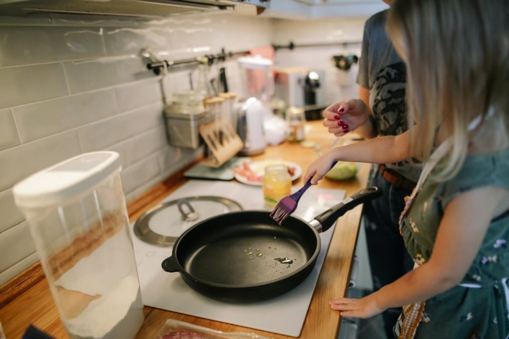 Child standing at the stove with a skillet and a pastry brush.