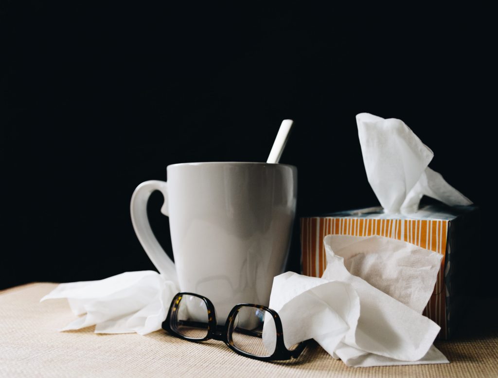 Coffee mug, glasses, and used tissues next to a tissue box