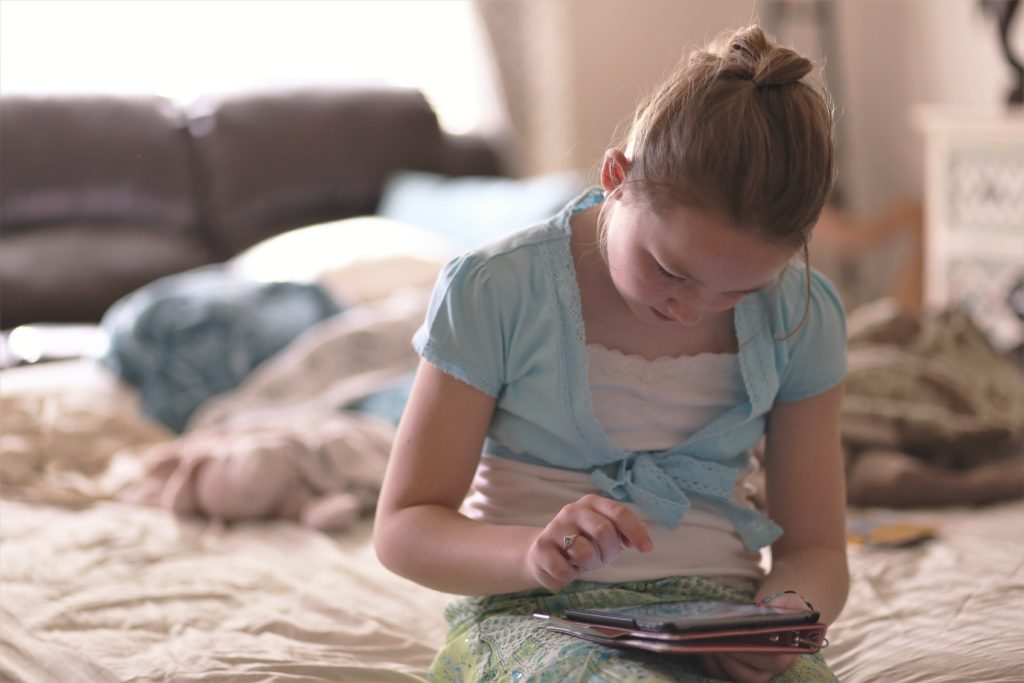 Child sitting on a bed using a tablet