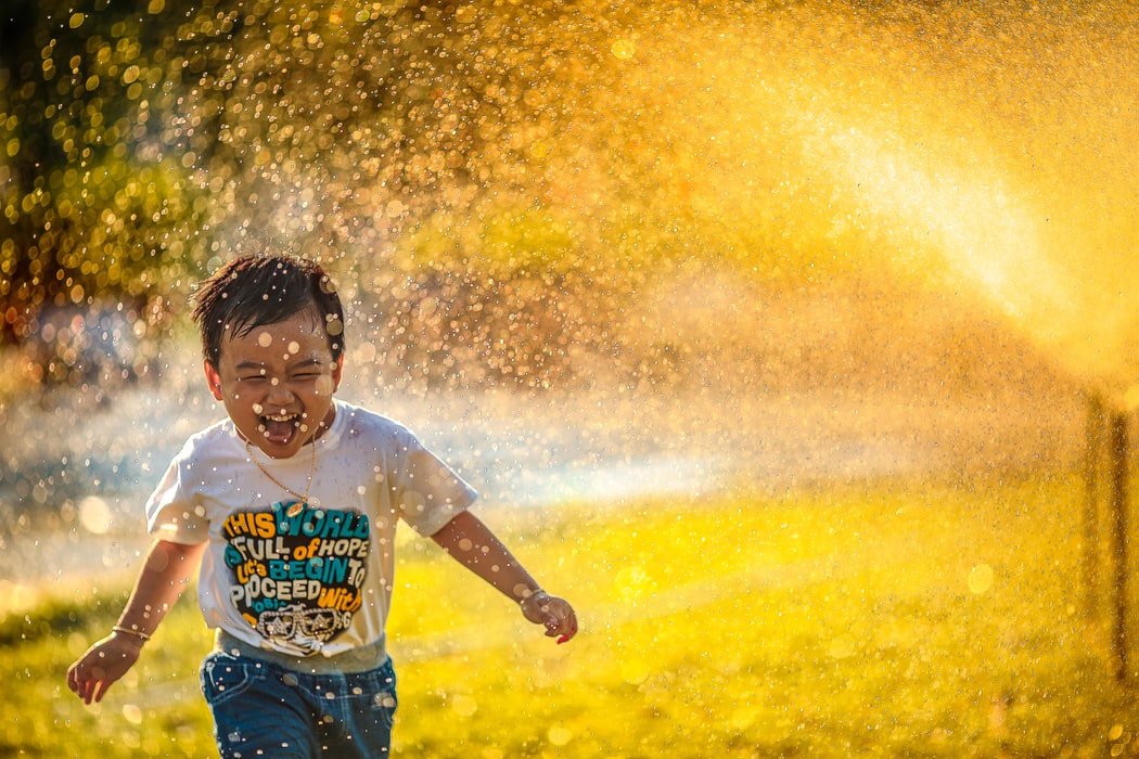 Child running through sprinkler with large smile
