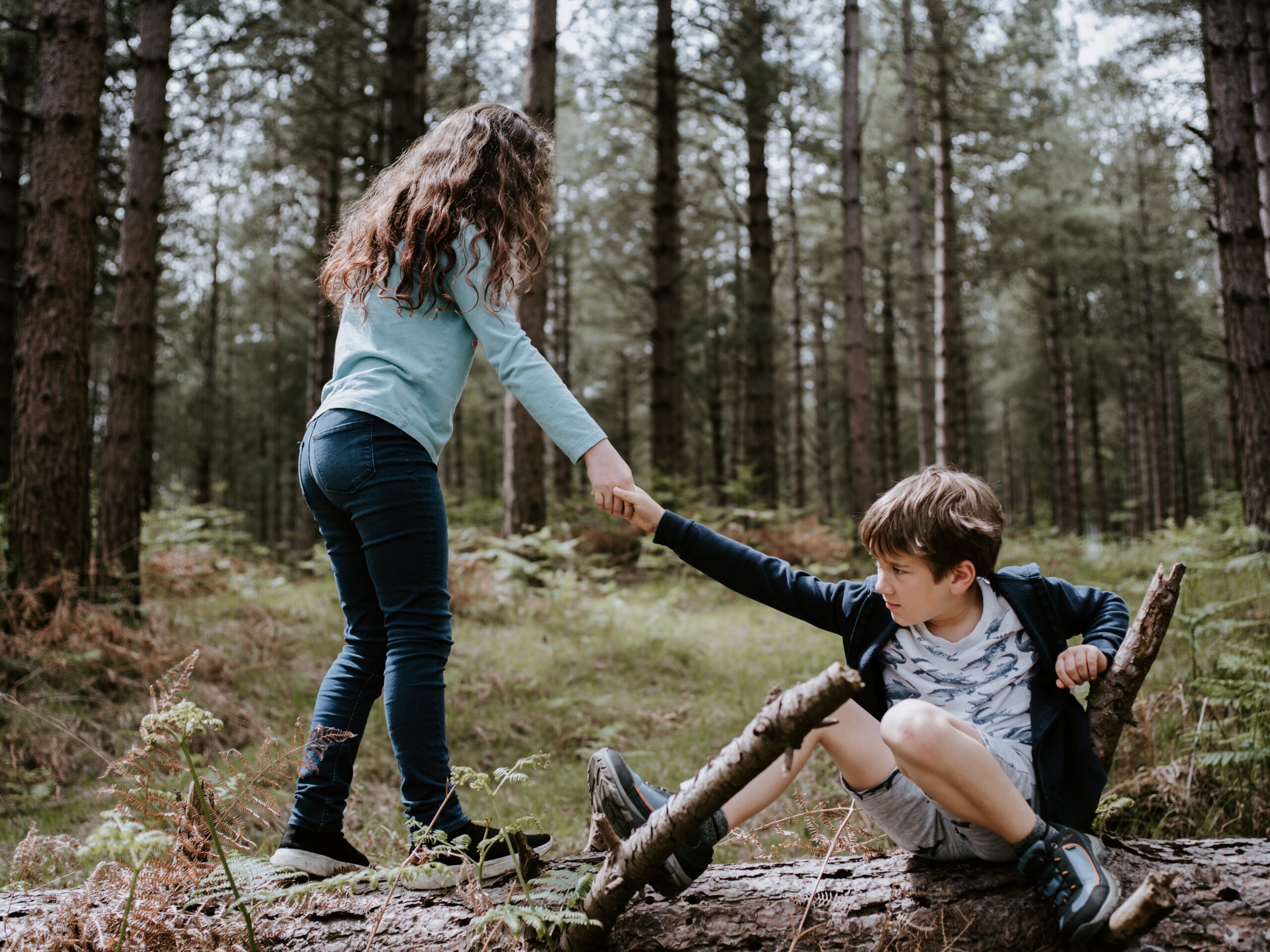 Girl helping boy up from log