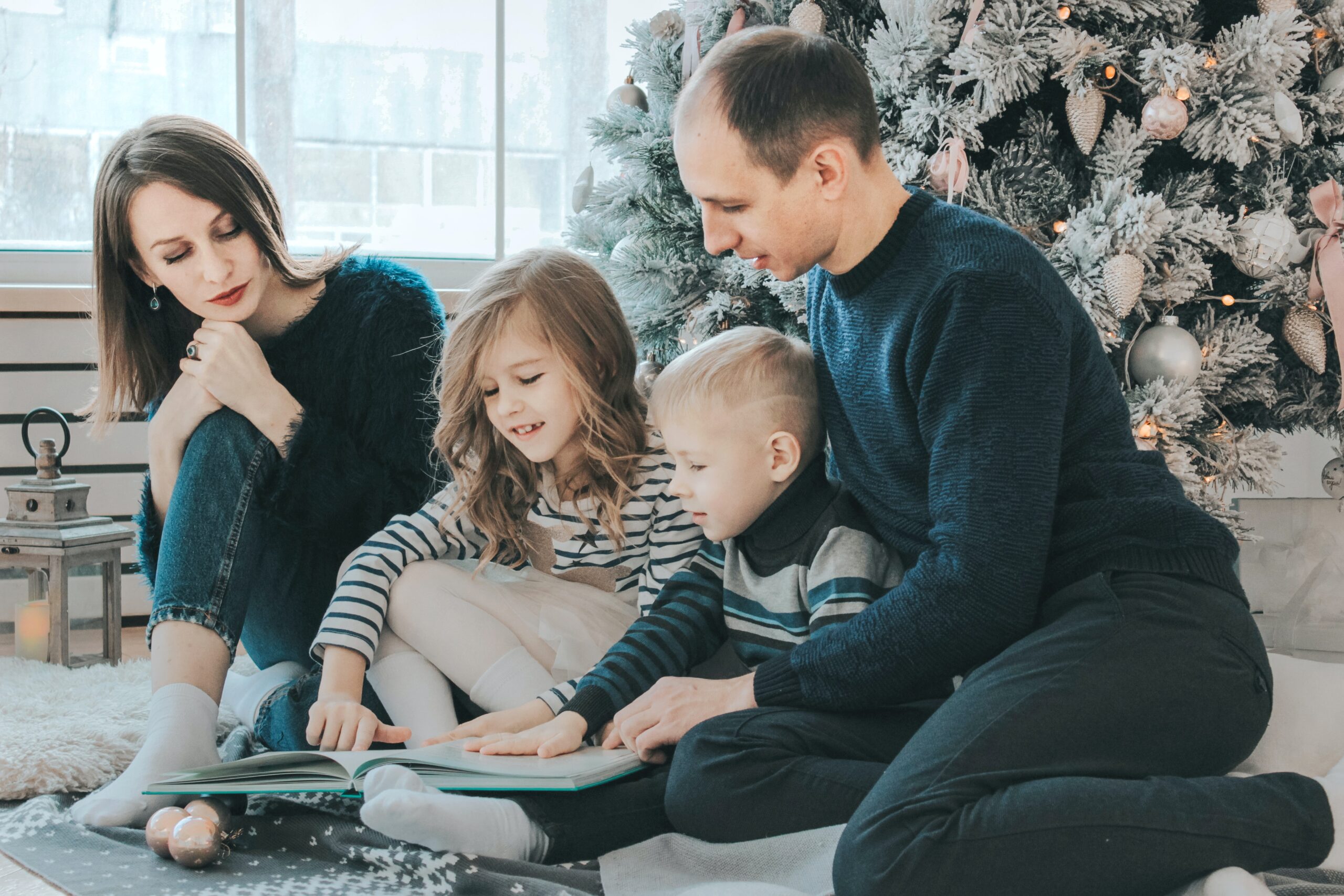 Family reading a book in front of Christmas tree 2